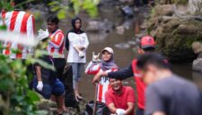 Di tengah rimbunnya tepian sungai, para pemuda yang mengenakan pakaian bernuansa merah-putih dan atribut relawan tampak melempar senyum serta pose penuh semangat ke arah kamera.