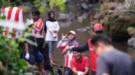 Di tengah rimbunnya tepian sungai, para pemuda yang mengenakan pakaian bernuansa merah-putih dan atribut relawan tampak melempar senyum serta pose penuh semangat ke arah kamera.