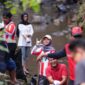 Di tengah rimbunnya tepian sungai, para pemuda yang mengenakan pakaian bernuansa merah-putih dan atribut relawan tampak melempar senyum serta pose penuh semangat ke arah kamera.
