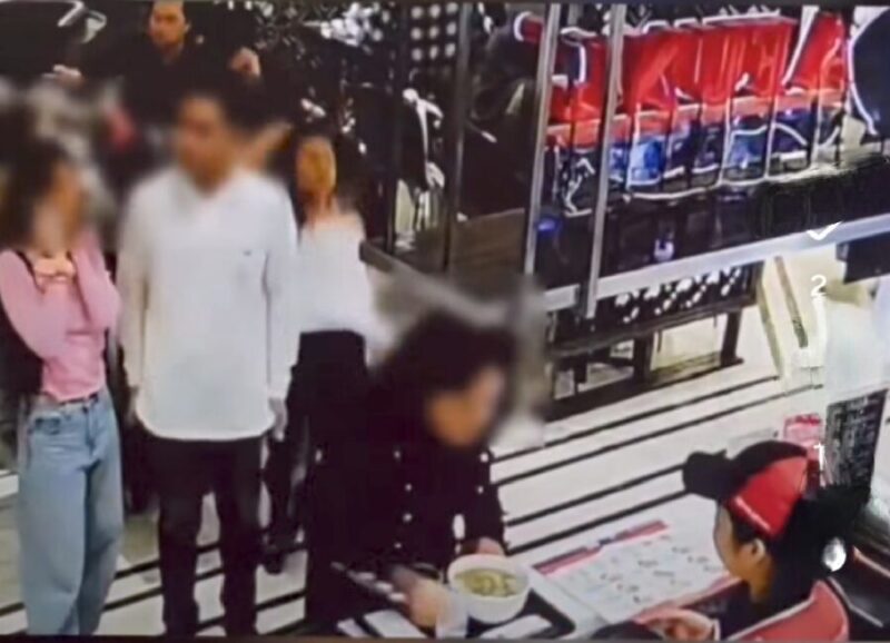 Tangkapan layar video viral di medsos, seorang wanita (berdiri mengantre paling kanan) ditendang pria berbaju hitam yang duduk di belakangnya.